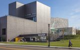 A person walking on a sidewalk in front of the entrance of a gray modern-shaped building, the Walker Art Center.