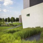A large grey building next to a smaller white building with a rhombus shaped window next to grass and trees on a sunny day