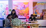 Adults looking down and smiling at a table with art supplies and colorful cartoons on the wall