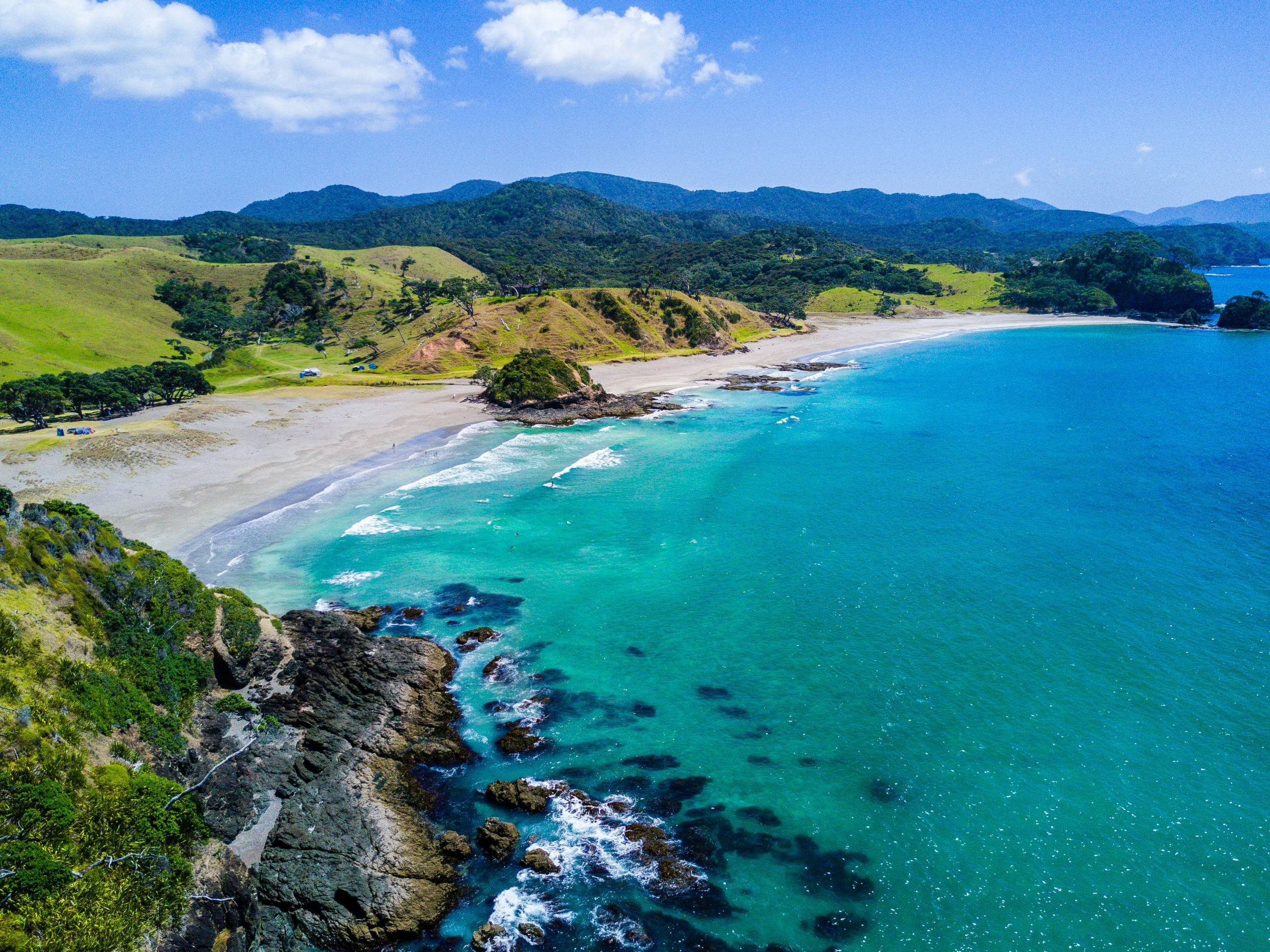 A high angle view of a coastline with crystal blue waters and lush green hills beyond the sandy beach