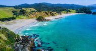 A high angle view of a coastline with crystal blue waters and lush green hills beyond the sandy beach