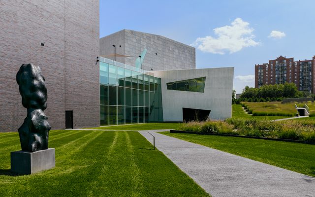 The back of the Walker Art Center with a large grass yard and a art sculpture on a sunny day.