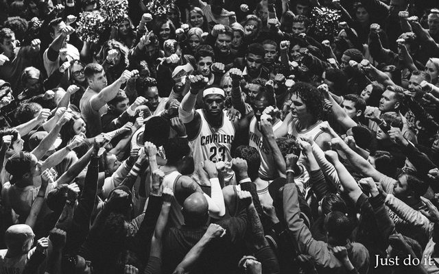 A black and white image of Lebron James with his fist raised in the center of fans and teammates with their first raised towards him, with the text reading 