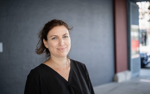 A fair skinned woman with brown hair and a black shirt smiling and posing for a photo