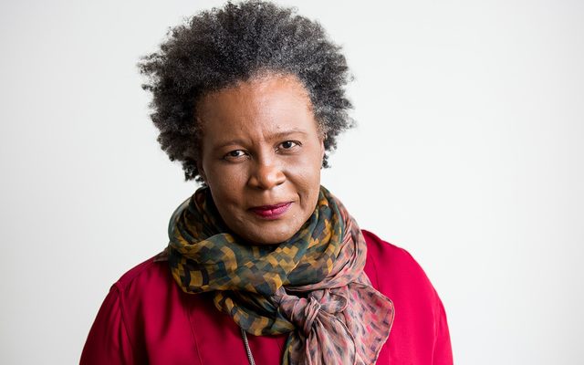 A darker complexioned adult with short black hair and wearing a patterned scarf and red shirt