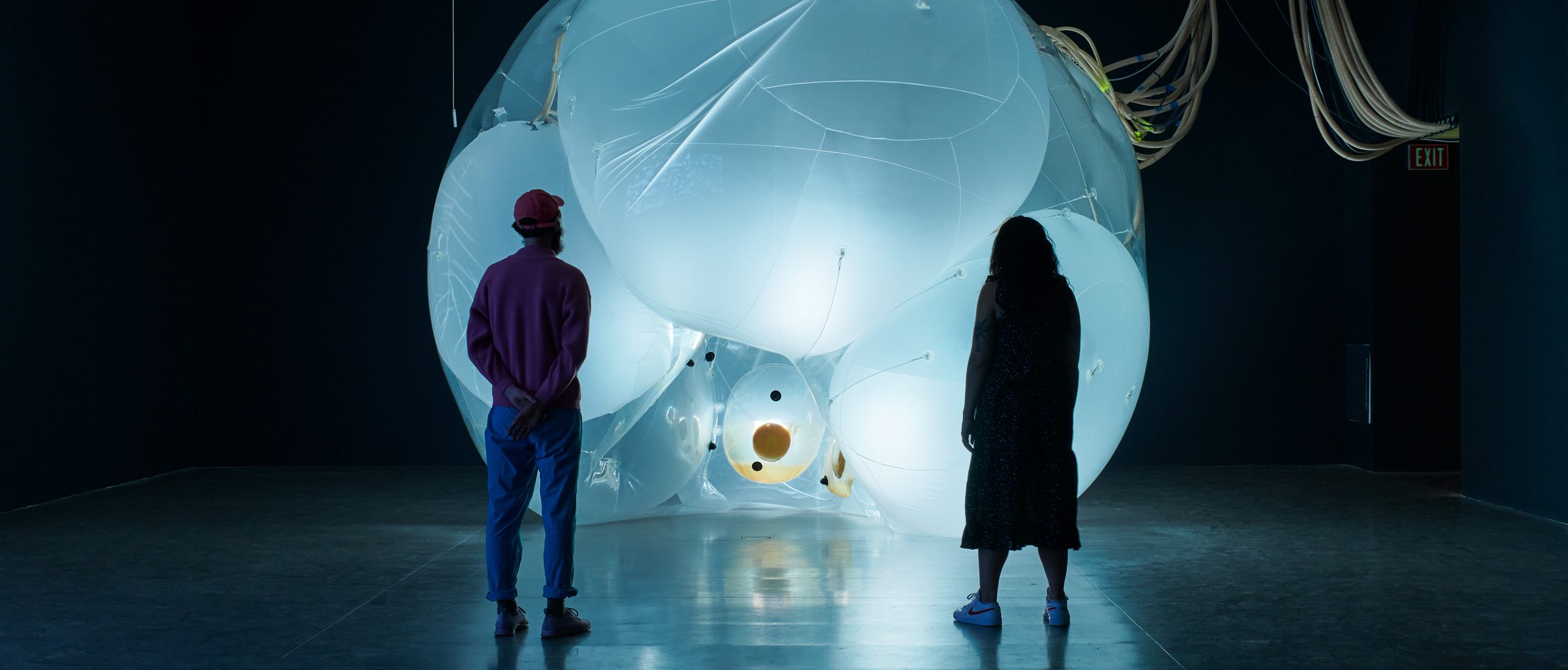 Two adults looking at a large illuminated and inflated art installation in a dark room