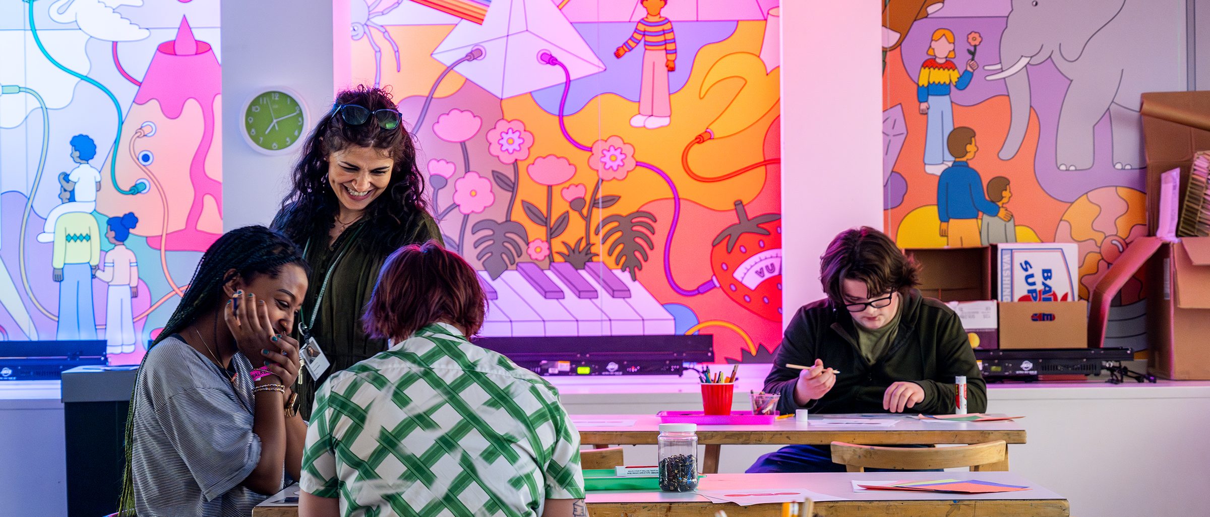 Adults looking down and smiling at a table with art supplies and colorful cartoons on the wall