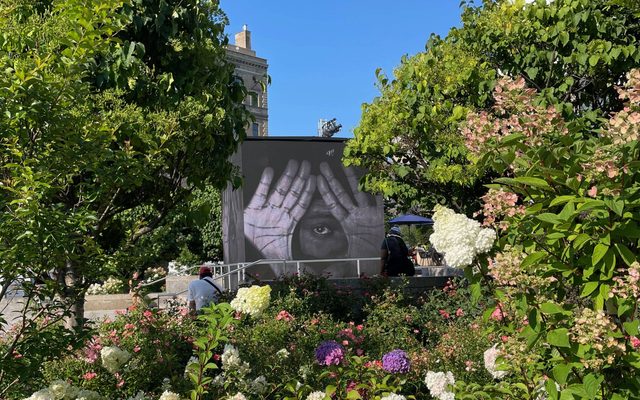 A garden with a food truck behind some trees with a mural of hands and eye.