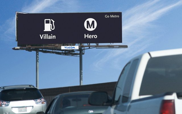 A highway billboard high in the blue sky, with a black background and white logos: Gas logo with the text 