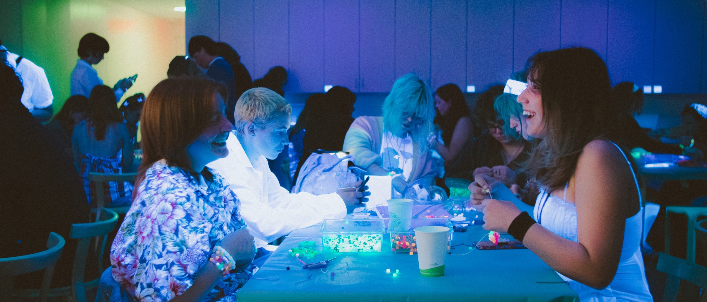 People sitting at tables, making glow-in-the-dark crafts in a blacklit room