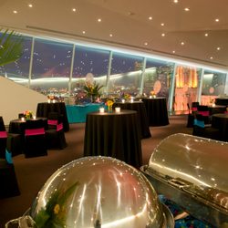 Inside of an empty and dressed dining area, with big windows, black cloth, pink and blue accents and silver serving trays at night