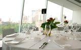 Round dining tables with white table cloth bearing silverware, wine glasses, plant center piece, and a black table sign reading 