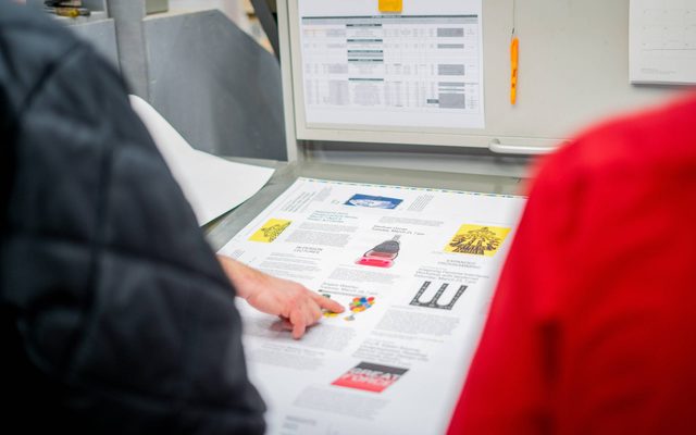 A hand pointing to a printed sample on a table