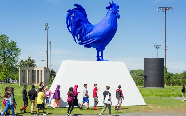 A group of adolescents walk past and outdoor art structure of a large blue rooster