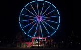 Ferris wheel outside at night, covered in colorful lights with a platform of guests standing in line for the ride
