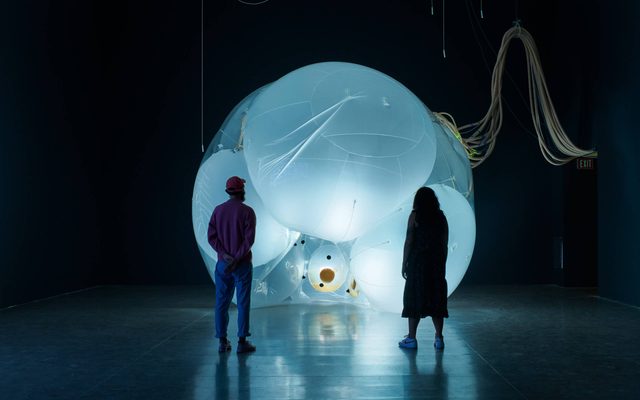 Two adults looking at a large illuminated and inflated art installation in a dark room