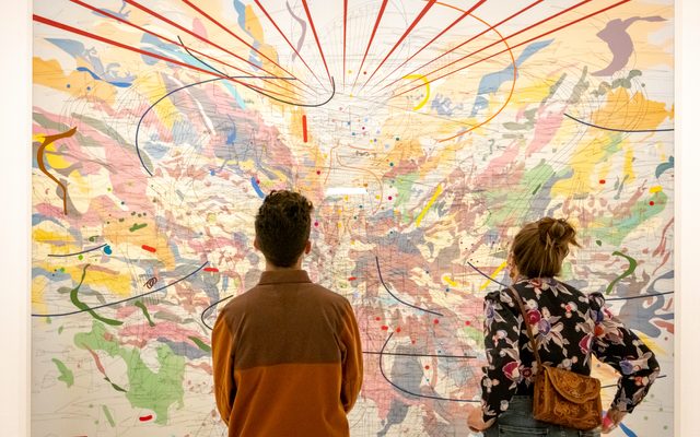 A view from behind two adults looking at a wall sized art map