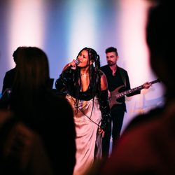 A singer and guitarist performing in front of an audience in front of a lit backdrop