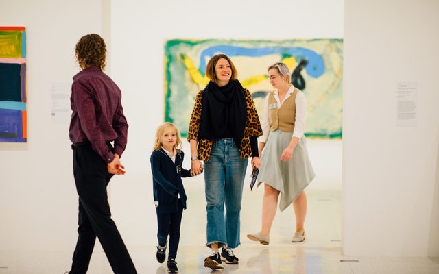 An adult holding an adolescents hand while walking through a museum with other visitors walking around.