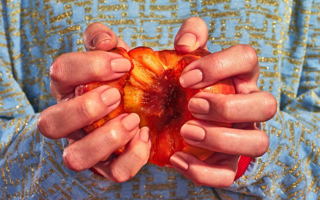 A person with a gold and blue sure holding a partially opened peach