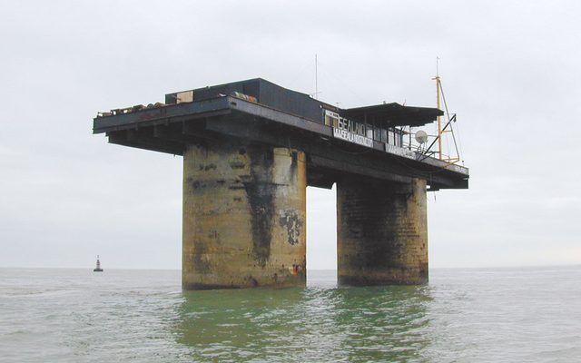 An off-shore platform in sea water with a sail boat in the background