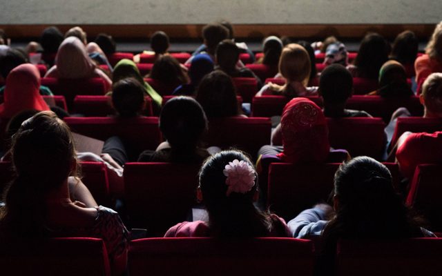 The backs of teens' heads are seen in cinema seats as they watch a film.
