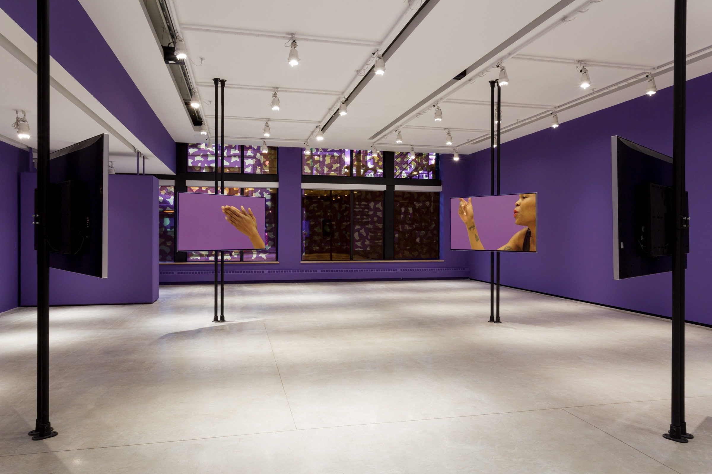 Four large screens are mounted on vertical black bars. Each shows a Black woman in motion,