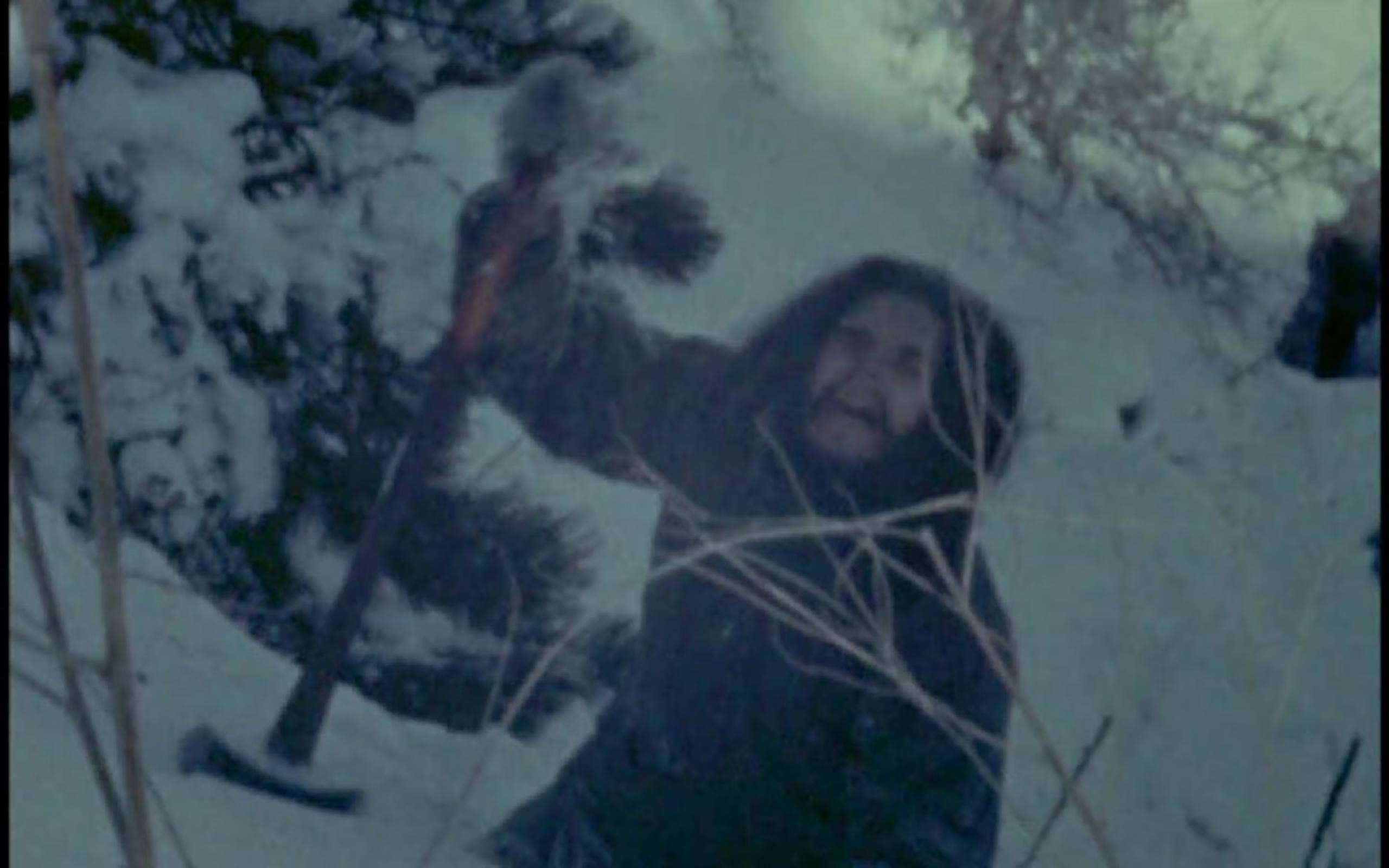 A blurry still frame shows a bundled-up man with an axe, trying to mount a snowy hill.