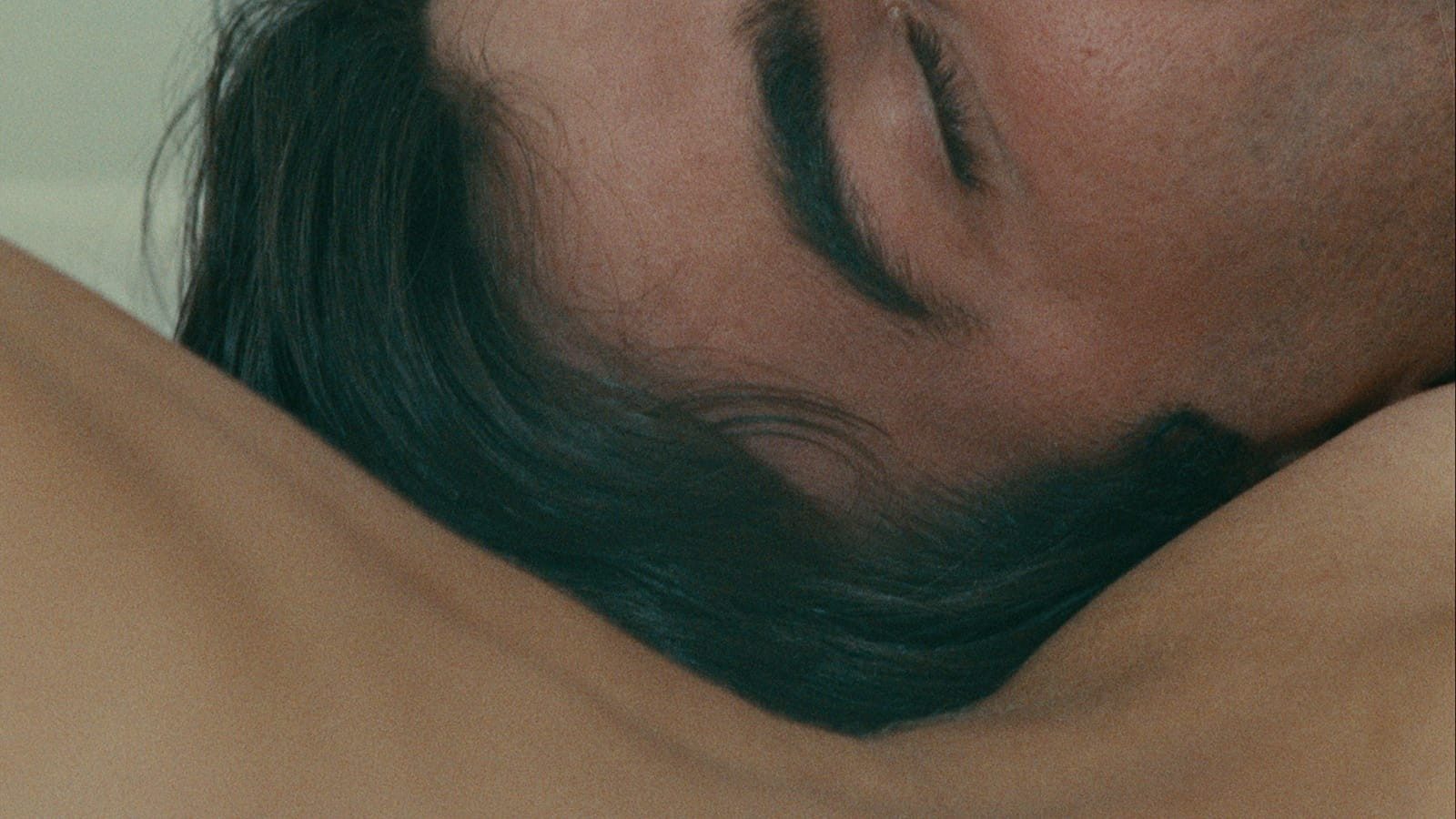 A very close cropped shot of a mans head with brown hair and eyes closed resting against the curve of a woman's nude back.