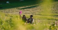 two people sitting in the grass on the Walker Art Centers hillside. One is holding a fan.