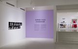 A contemporary art gallery displays a lavender wall with the title SOPHIE CALLE OVERSHARE and descriptive text; nearby are black-and-white photo artworks and, on a higher level, installations including a pink dress and furniture.