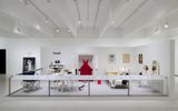 Museum exhibit features household objects, clothing, and art pieces displayed in a well-lit, modern gallery space.