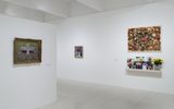 Gallery with white walls displaying framed artwork and photographs, plus a shelf with potted flowers and photos.
