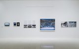 A white gallery wall displays various landscape and abstract photos in different sizes, arranged in a neat row.