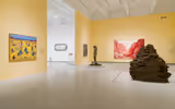 A gallery space with a mountain-like sculpture and paintings on the wall.
