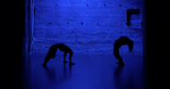a room with a brick wall lit with a deep blue hue featuring two silhouette figures dancing