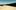 A landscape shot of the desert at the U.S. – Mexico border, looking down along a dark black border wall that disappears into the vanishing point.