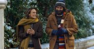 A woman and a man in winter coats and scarves walk together outdoors in the snow.