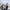 Three adults, two men on either side of a woman, in business attire stand outside on a rooftop with a city skyline in the background. The sky is clear and it's sunny.