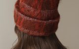 A person wearing a fuzzy, rust-colored knit beanie with a folded cuff.