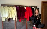 A woman in a black sweater and trousers sits on a red stool in front of a folding screen displaying several colorful cardigans.